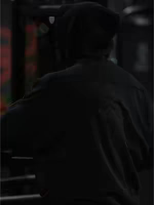 The image shows a person from the back, wearing a dark beanie and a dark shirt. The background is blurred and out of focus. The overall tone of the image is dark and moody.