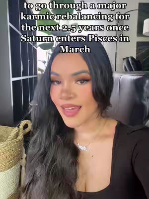 A well-lit selfie-style shot features a woman with long, dark hair. She is positioned slightly off-center, looking towards the camera with a smile. The background includes a shelf and a bit of the room, suggesting a home setting. The text overlay at the top announces a karmic rebalancing.