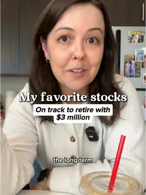 A woman is shown in a selfie-style video. She has brown hair and is wearing a white sweater and a small clip-on microphone. Text overlays identify her favorite stocks and her goal of retiring with $3 million. The background includes a refrigerator, a kitchen, a clear cup with a red straw, and a smartwatch on her wrist.