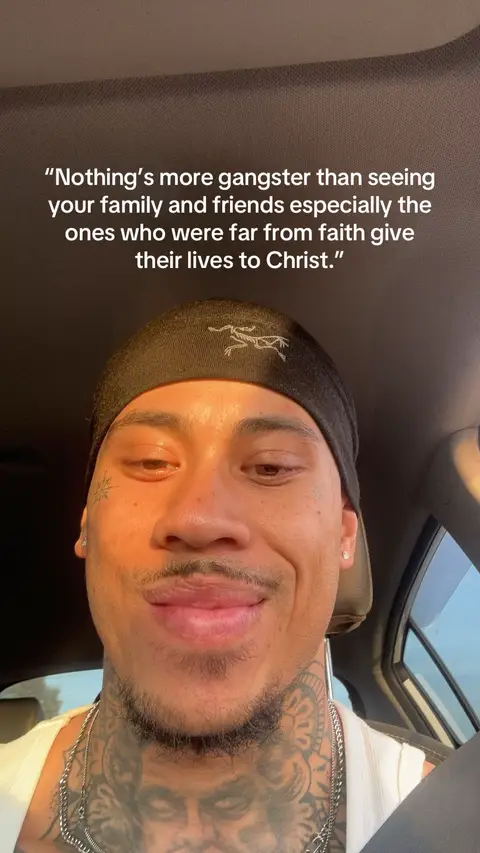 A selfie-style video cover image featuring a man smiling. He is wearing a black head covering, a white tank top, and has arm tattoos. Text overlaid on the image includes a quote about faith and family.