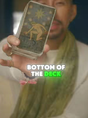 A person holding a deck of tarot cards, with a text overlay at the bottom. The person appears to be in the foreground, dressed casually with a green scarf. The background is slightly blurred, suggesting an indoor setting. The photo has a warm and slightly desaturated color palette.
