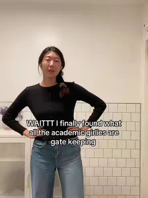 A young woman with dark hair and wearing a black long-sleeve shirt and blue jeans stands facing the camera, hands on her hips. Text overlayed on the image reads, "WAITTT I finally found what all the academic girlies are gate keeping"