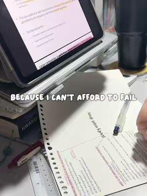 A desk setup with a tablet displaying notes, a notebook with handwritten text, a pen, and other stationery. The background is slightly blurred, giving focus to the workspace.