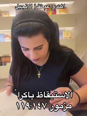A woman with long dark hair, wearing a necklace with a cross pendant, is looking down at a book, probably the Bible. Text overlays in Arabic and English are present on the image.