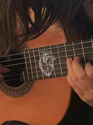A person's hands are shown playing a guitar. The body of the guitar is brown, and the fretboard is dark with a white anatomical heart displayed on the fretboard at the point where the strings and the frets meet.