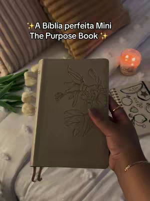 An overhead shot of a well-lit bed with pillows, a green plant, and a beige book being held by a hand with a gold bracelet. A lit candle is in the background. The cover image has text overlay.