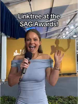 A woman with light skin and brown hair, wearing a gray, off-the-shoulder dress, holds a microphone and expresses excitement in front of a gold backdrop. Text at the top reads, 'Linktree at the SAG Awards!'