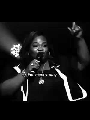 A black and white image of a woman performing on stage, holding a microphone and singing with her right arm raised. The background is blurred with stage lights. Text overlayed on the image reads, "You made a way".