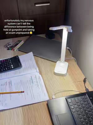 The image shows a desk setup ready for studying. On the wooden desk, there's a laptop, open study notes, a calculator, and a desk lamp. The lighting gives the scene a focused and serious atmosphere.