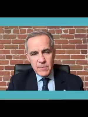A man in a dark suit and blue tie is seated in front of a brick wall. The frame includes a teal border at the top and bottom.