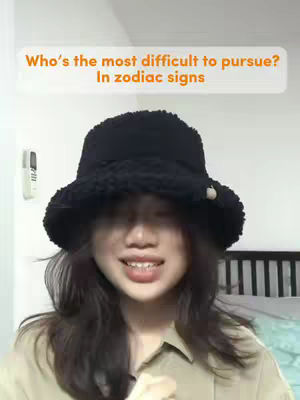 A young woman with long dark hair and a black fuzzy hat is smiling at the camera. An orange-colored text box floats above her head. The background is a blurred interior.