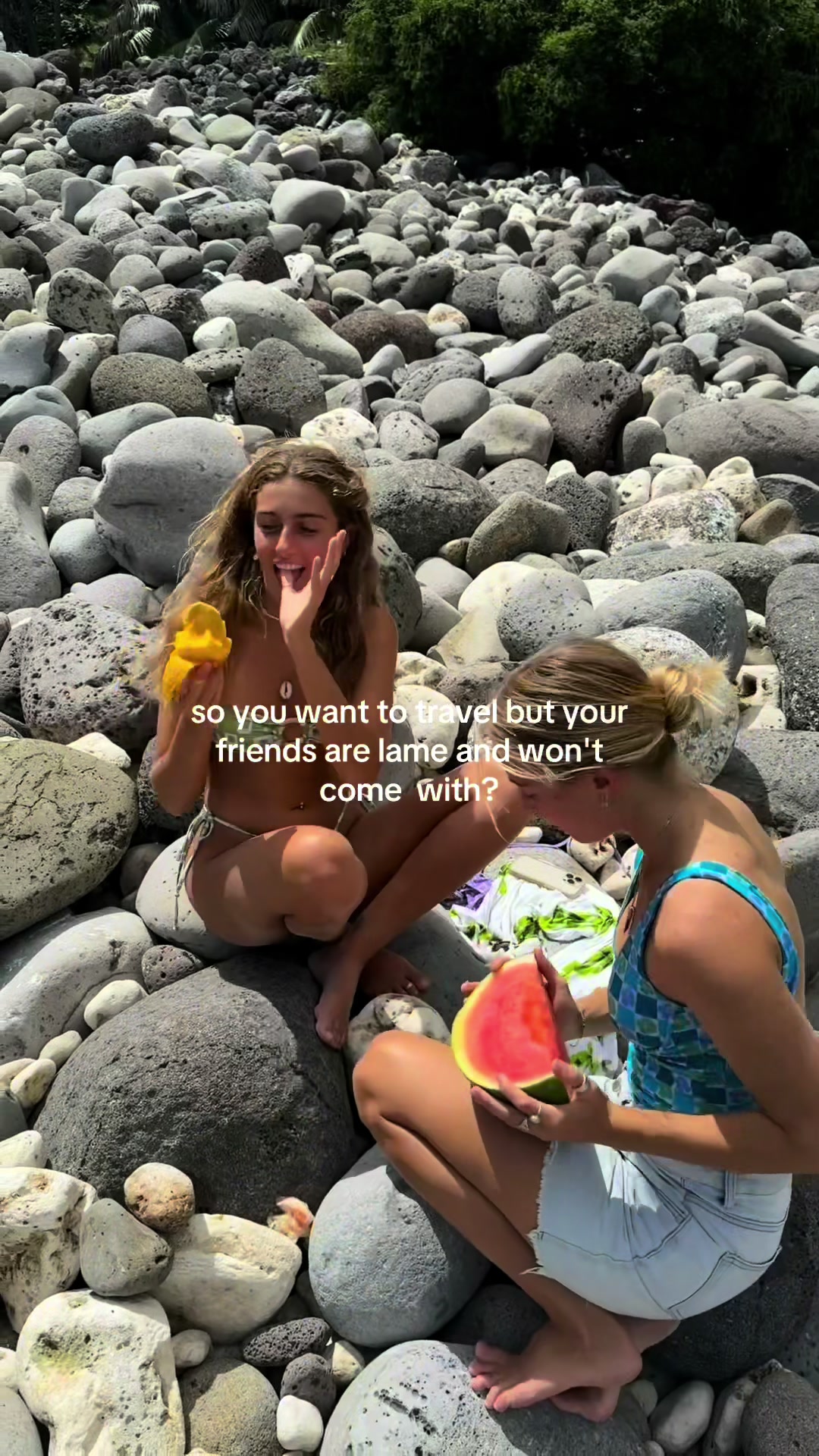Two young women are sitting on a rocky beach, one holding a piece of watermelon and the other a mango, with text overlaid on the image.