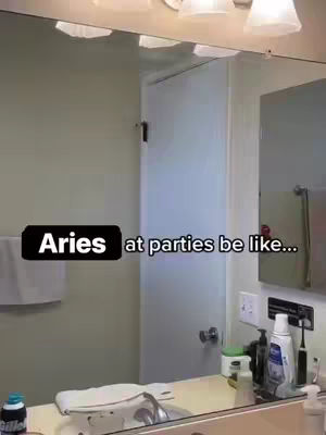 A person is reflected in a mirror in a bathroom. The text "Aries at parties be like..." is overlayed at the bottom of the image. In the mirror, toiletries are visible, the focus is on the text overlay.