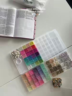 The image shows a top-down view of a table with materials for making bracelets, including containers of colorful beads, an open book, and a small bag.