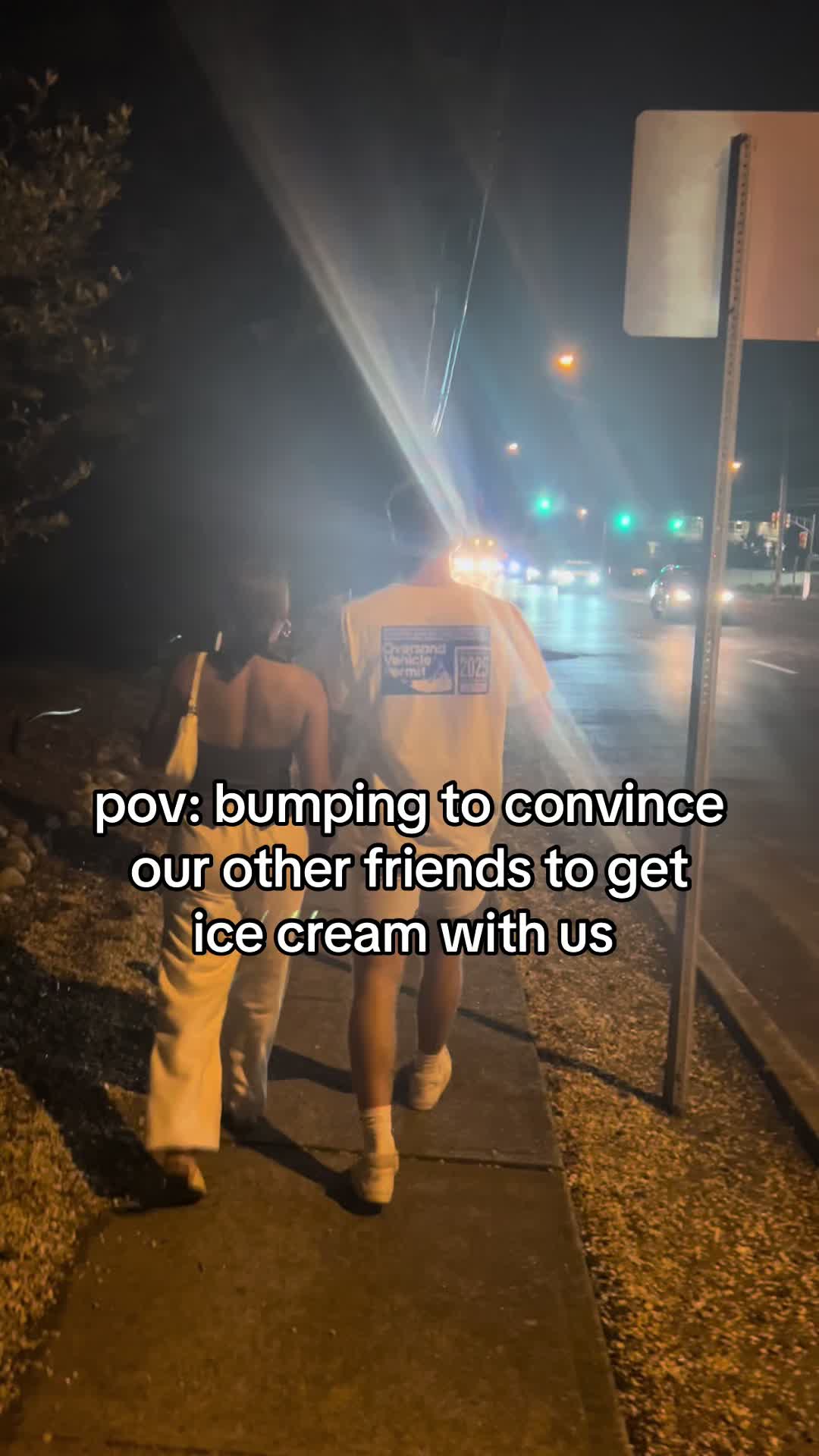 A nighttime shot featuring two people walking on a sidewalk away from the camera, likely a couple, with a dark background and streetlights visible. Added text overlay.