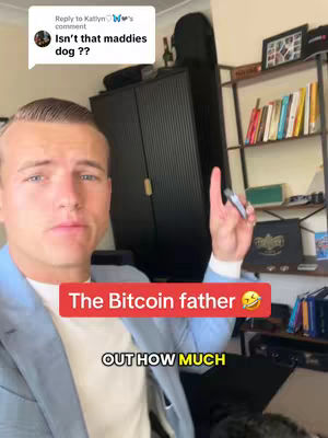 A man in a light blue blazer and white t-shirt is in the foreground, pointing upwards with one hand while holding a pen. He is centered and looking at the camera with a serious expression. Overlayed is a red box with white text that reads: The Bitcoin father with a laughing emoji. Beneath it is the text: OUT HOW MUCH. The background includes a dark cabinet, a bookshelf with books, and items such as a small framed picture are visible on the shelf.