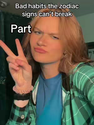 A selfie-style video cover featuring a young woman. She has light-colored hair and is wearing a blue shirt under a green plaid jacket. She is making a peace sign with her fingers, and the text overlay at the top says 'Bad habits the zodiac signs can't break' and the word 'Part' at the bottom left.