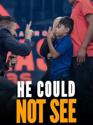 A cover image with a dark background featuring a large white and orange text overlay that reads "HE COULD NOT SEE". In front of the text, three men are visible: one on the left gesturing with two fingers, another in the center partially obscured, covering a young boy's eyes, and the third on the right with red shirt, partially cut off. The boy in the center is wearing a blue polo shirt, and a man next to him has his hand cover his head.