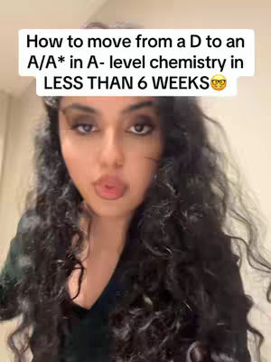 A selfie-style video cover featuring a young woman with long, curly black hair. She has prominent makeup, including dark eyeshadow, and is making a kissing face. Above her, a white rectangular text box displays the video's title, which discusses improving A-Level chemistry grades. The background appears to be an interior space.