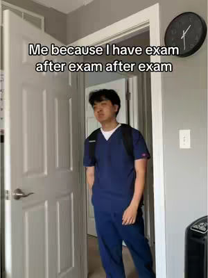 A young man in a navy blue scrubs stands in a doorway, looking somewhat forlorn. The background shows a room with a white door, a black clock, and light gray walls. The lighting is natural, coming from the room and brightening the man's face. He has a backpack on, suggesting a student or professional on the go. The hook text is overlaid on top and reads: Me because I have exam after exam after exam.