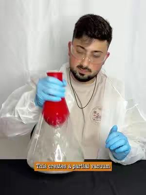 A man in a lab coat and safety glasses is holding a red cup in an inverted clear flask-like container. The background is plain and white. Text is added to the bottom.