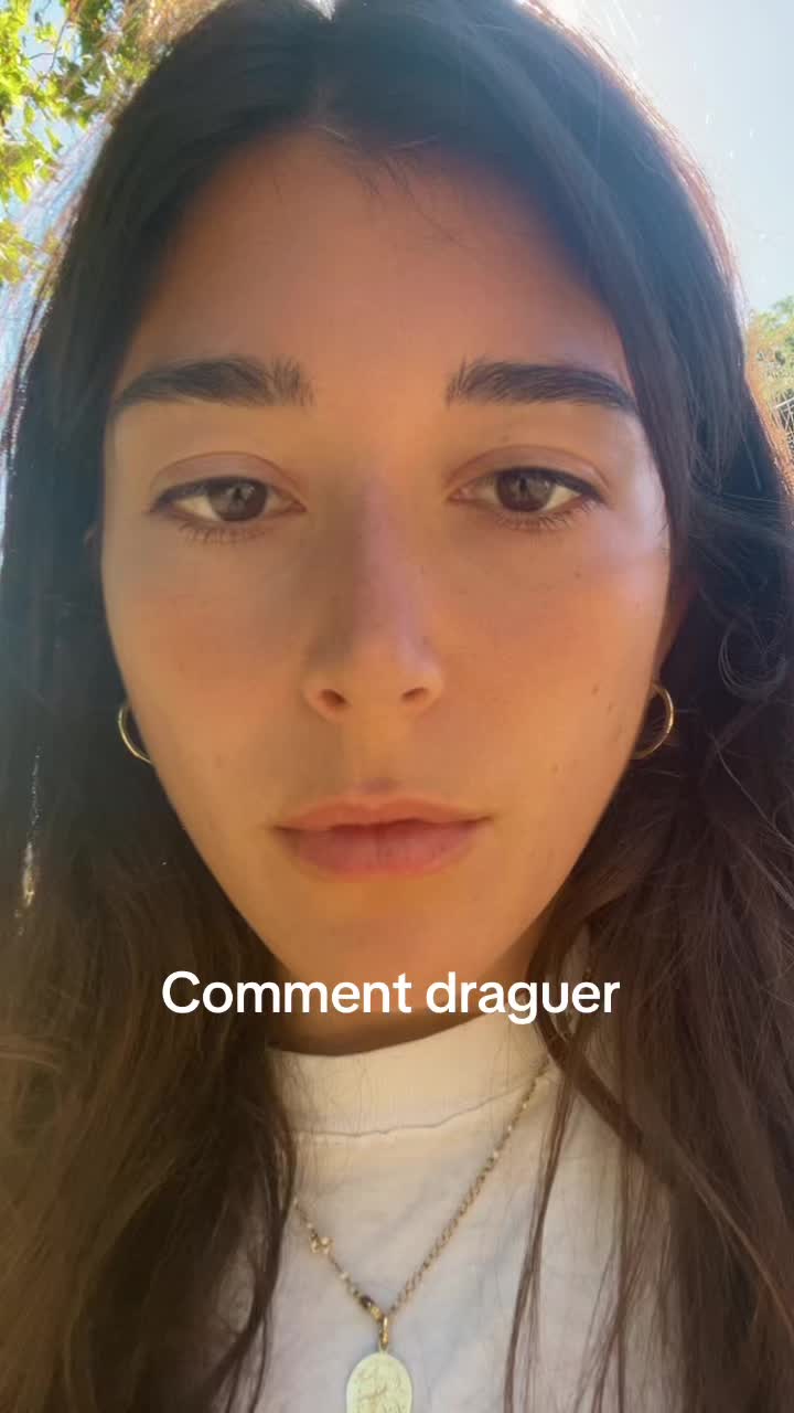 A close-up shot of a young woman's face fills most of the frame, with a soft, natural light illuminating her features. She has dark, wavy hair framing her face and is looking directly at the viewer with a neutral expression. Her skin appears smooth, and she wears small gold hoop earrings. The text overlay is in white, positioned below her face.