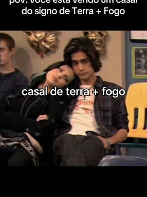 The image features a couple, a man and a woman, in a room. The man is wearing a plaid shirt with a white t-shirt underneath and is looking forward. The woman is leaning on the man's shoulder, her eyes closed, and both seem relaxed. The caption 'casal de terra + fogo' is written on the screen. The background is a blurred room.