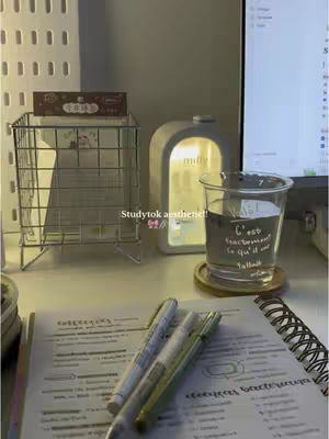 A well-lit, aesthetically pleasing workspace with a notebook, pens, and a glass of water. The scene is dominated by warm lighting, creating a cozy atmosphere.