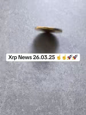 A shallow depth-of-field shot featuring a spinning gold coin, centered with its shadow. Below the coin is a white rectangular text overlay. The background is a simple gray surface.