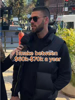 A man wearing sunglasses and a black vest is being interviewed on a city street. Text overlayed on the image states, \"I make between $60k-$70k a year.\"
