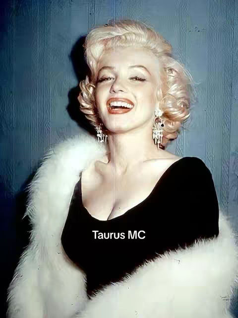 The cover image features a vintage photograph of Marilyn Monroe. She is smiling with her head slightly tilted. Her blonde hair is styled in soft waves and curls, and her eyes are bright. She is wearing a black dress that shows cleavage and a glamorous white fur stole. The background is a textured teal color. In the bottom center, the text "Taurus MC" is superimposed.