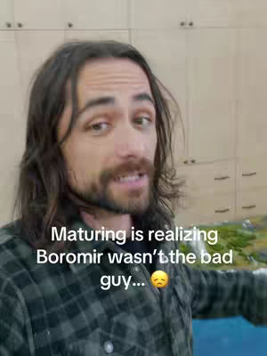 A man with long hair, a beard, and a plaid shirt is centered in the frame. Text overlays are present, and the background shows a neutral-toned wall.