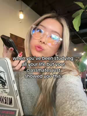 A selfie-style shot featuring a young woman wearing glasses and holding a phone. The background includes an out-of-focus setting, while overlaid text shares a relatable student experience.