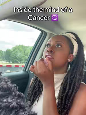 A woman in a car interior looks up with a contemplative expression, her finger touching her lip. Overlayed is the text "Inside the mind of a Cancer" with the Cancer zodiac symbol.
