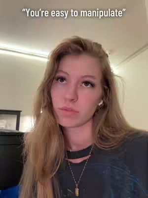 A close-up shot of a young woman looking up with a slightly skeptical or contemplative expression. Above her head is white text against the background. She has long blonde hair, wearing a dark top, a necklace, and small wireless earbuds.