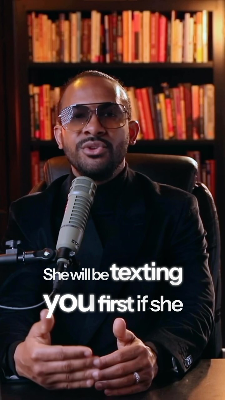 A man in a black blazer and sunglasses is speaking into a microphone. Text is overlaid on the image.