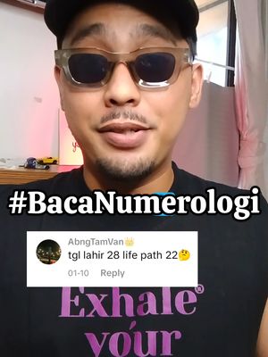 A selfie-style video cover featuring a man wearing sunglasses and a black cap. He is in a well-lit room with a white wall in the background. Overlayed on the image is a text that says '#BacaNumerologi', and a comment box excerpt with text regarding a birth date and life path.