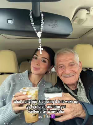 A selfie taken inside a car featuring a young woman and an older man, both smiling and holding coffee cups. The background includes the car's interior, a rosary hanging from the rearview mirror, and text overlays.