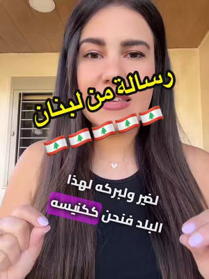 A woman with long dark hair is centered in the frame, smiling while holding a phone. The background is a plain wall. Overlay text in yellow Arabic is present along with several Lebanese flags. The overall composition is well-lit and focused on the person.
