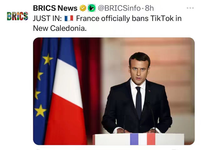 The image shows a news post about France officially banning TikTok in New Caledonia. It features a formal photo of a man, presumably a political figure, standing behind a podium with flags of France. The background has dim colors in the red/orange palette.