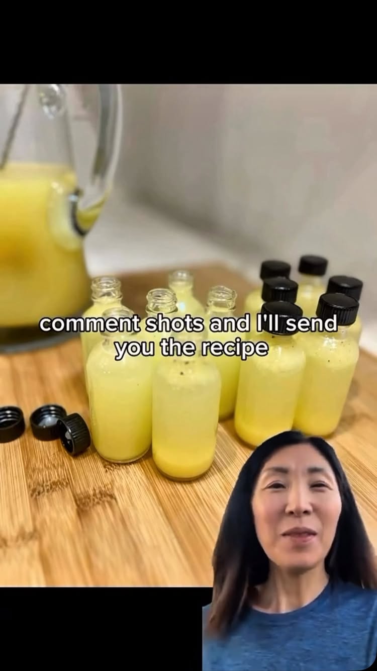The cover image shows a woman with dark hair and fair skin. In the foreground, there are several small glass bottles filled with a yellow liquid, arranged on a wooden surface. The text overlay reads 'comment shots and I'll send you the recipe.' The background includes a kitchen setting apparent from the mixer.
