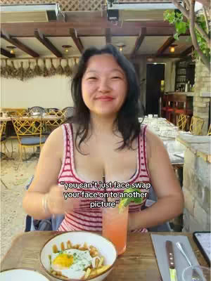 A woman is smiling at a restaurant, with a plate of food and a drink in front of her. The background has lights.