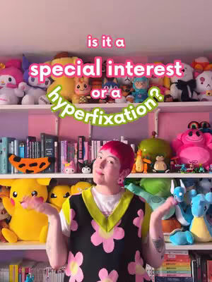 A person with pink hair stands in front of a shelf filled with plush toys and books. The person has their arms open to the side, with a smiling expression. Overlay text that reads "is it a special interest or a hyperfixation?" arcs over their head in between the shelves. The overall aesthetic is bright and colorful.