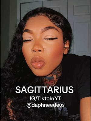A close-up shot of a Black woman with closed eyes and pursed lips, giving a kissy face. She has dark, wavy hair and is wearing a black top. The background is blurred neutral tones, and text overlaid identifies her as a Sagittarius.