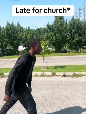 The cover image shows a Black man walking on an asphalt ground, with green trees and a road in the background, and a white text box overlay. He is dressed in a black outfit, walking in profile, and appears to be in motion. The sky is bright blue and the lighting is natural.