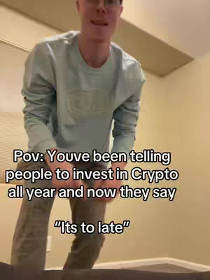 A man in a light blue long-sleeved shirt and glasses stands in front of a plain wall with overlaid text. The camera is positioned at a low angle, looking up at the man from the waist down. The man appears to be in a casual indoor setting, with a neutral background.