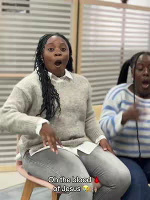 The cover image shows two Black women sitting on chairs and making expressions. The woman in the foreground has braided hair and wears a gray sweater over a white collared shirt and gray pants. She has her mouth open. The second woman on the right is making the same expression. A text overlay states, "Oh the blood of Jesus," and is accompanied by an emoji.