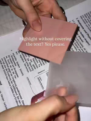 A hand holding a pink sticky note over a page of printed text, with a transparent sticky note layered over the text, showing a study technique.