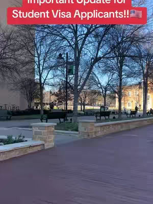 A photo of an outdoor scene on a sunny day, with a brick walkway in the foreground leading to a park. The background features buildings and trees. The sky is clear, and benches are lined along the pathway. A red banner with text overlays the top of the image.