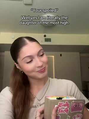 A woman in a light-colored top, smiling slightly, holds a book or device adorned with stickers. Text overlays float above her head, and the background suggests a well-lit interior.